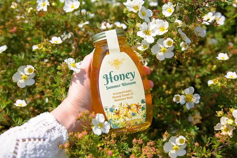 honeystickers_Events-summer Hand holding a honey bottle labeled 'Summer Blossom' amidst flowers