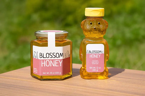 honeystickers_Soft-Sophie-Hexagonal-Bear-Jar-Sustainability Jar and bear-shaped bottle of Blossom Honey on a wooden surface with a blurred green background